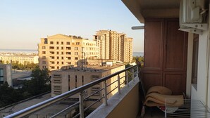 A balcony with a metal railing, a small seating area with a cushion, and a view of surrounding buildings. - Bakuvi Tourist Apartment B038 (Baku)