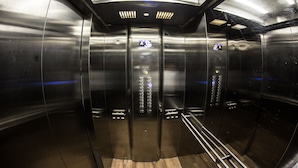 An elevator interior with metallic walls, a wooden floor, and control panels with illuminated buttons.