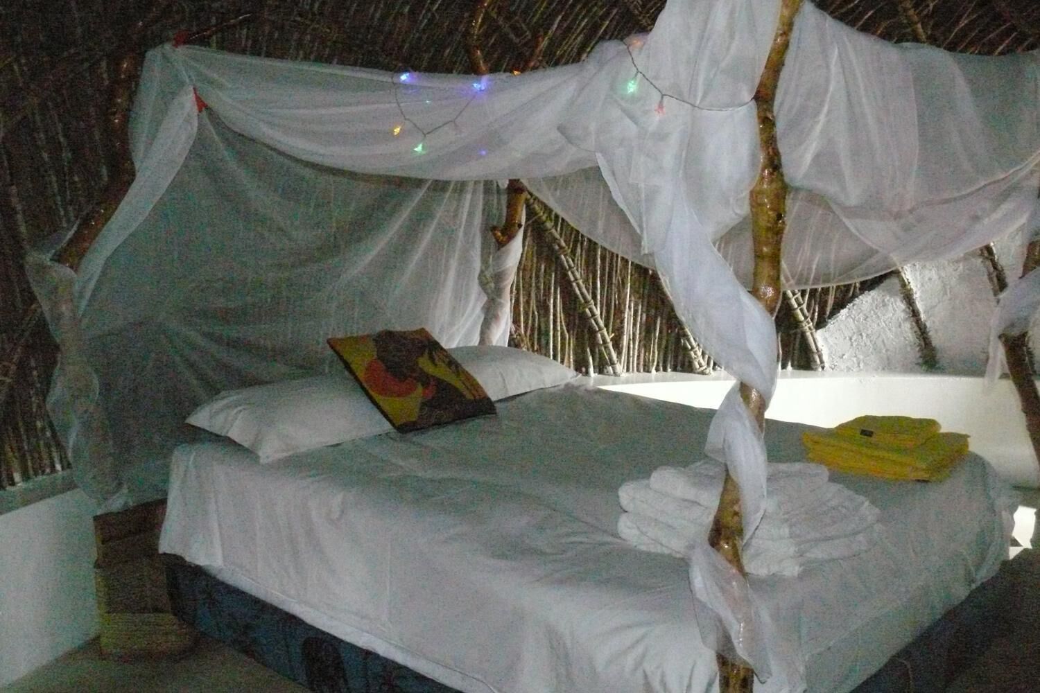 Una cama con dosel, un almohadón y una colcha.