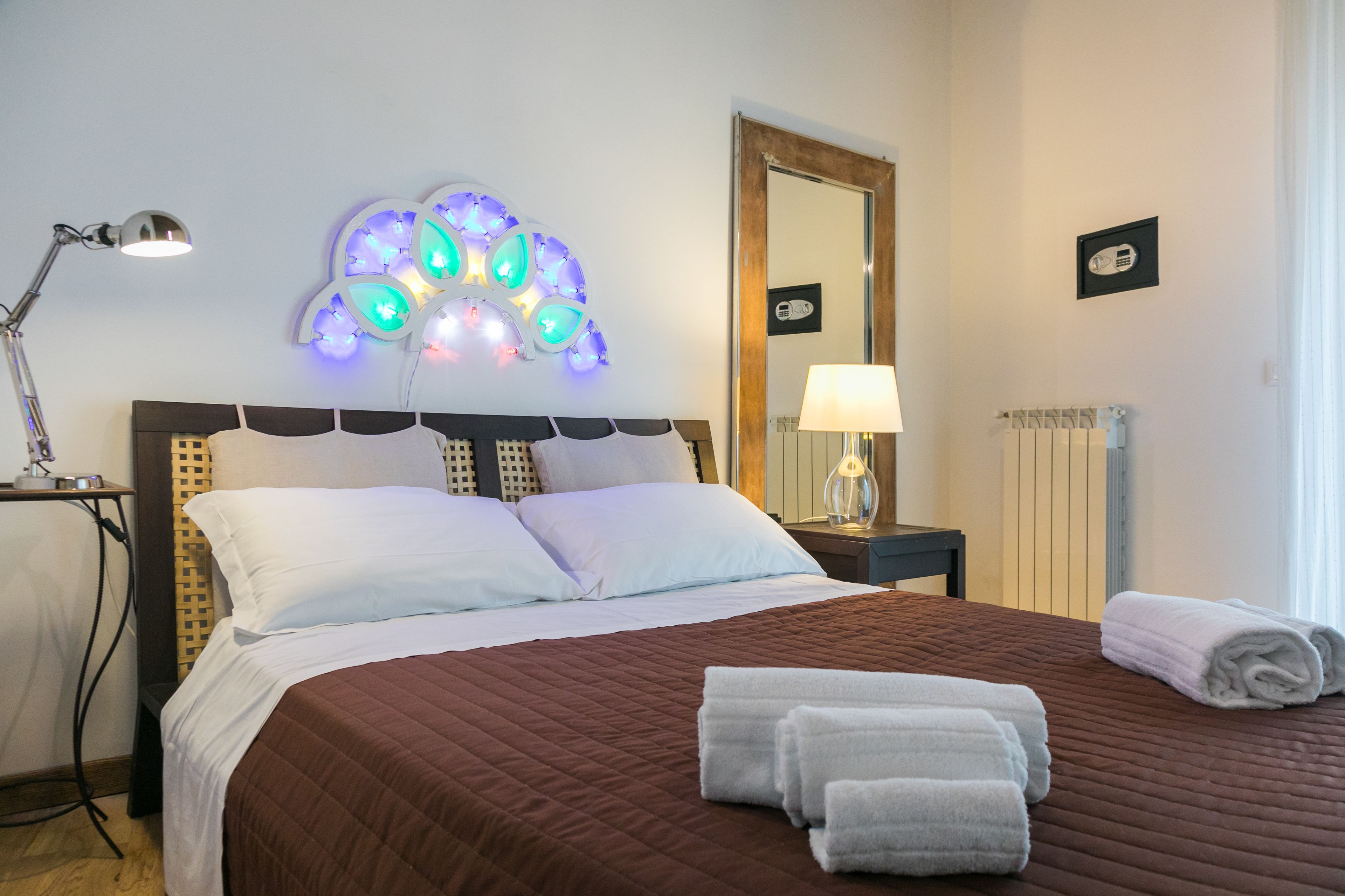 A neatly made bed with white and brown bedding, a bedside lamp, and decorative wall lights.