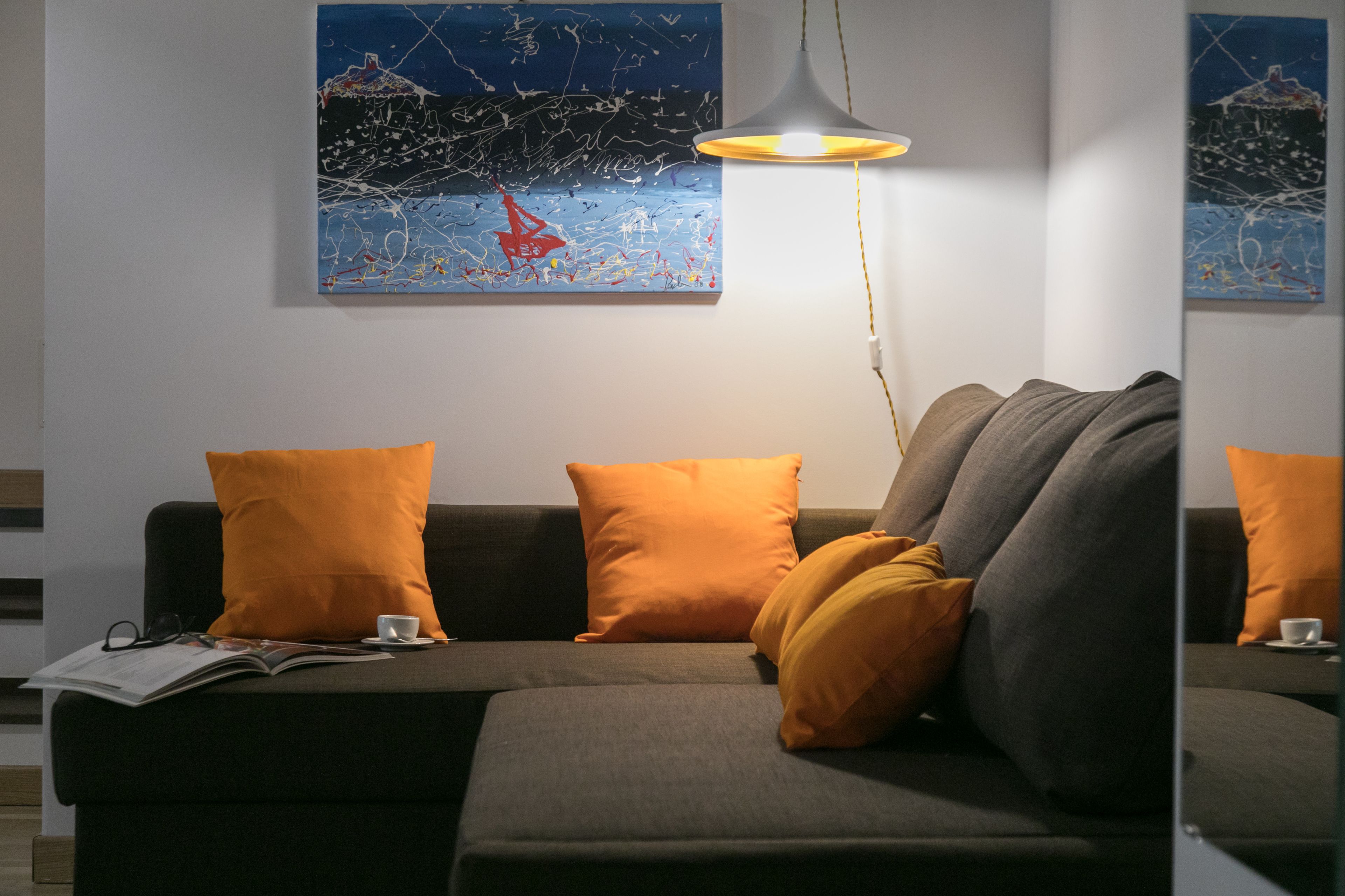 Ein modernes Wohnzimmer mit grauem Sofa, orangefarbenen Kissen und abstrakten Bildern an der Wand.