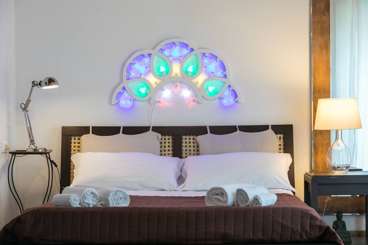 A neatly made bed with white and brown bedding, a decorative wall light, and a small statue on a nightstand.