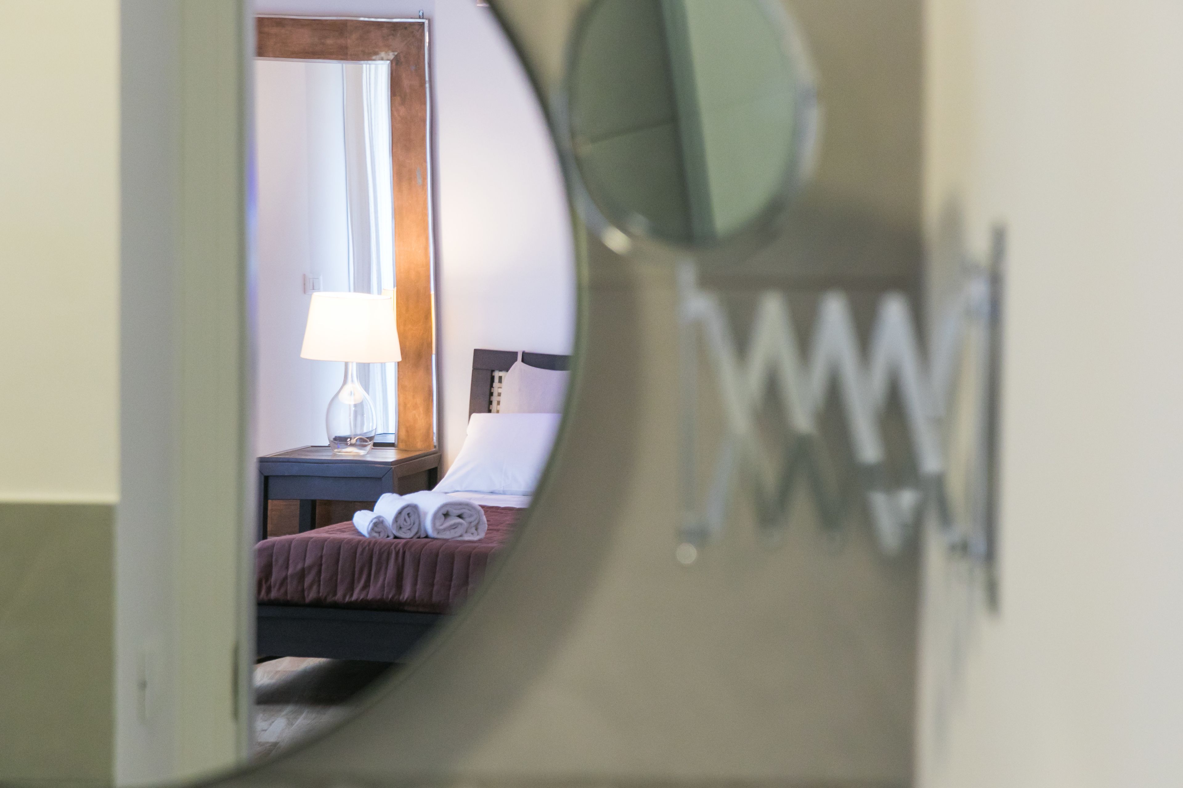Een slaapkamer met een bed, nachtkastje, lamp en spiegel.
