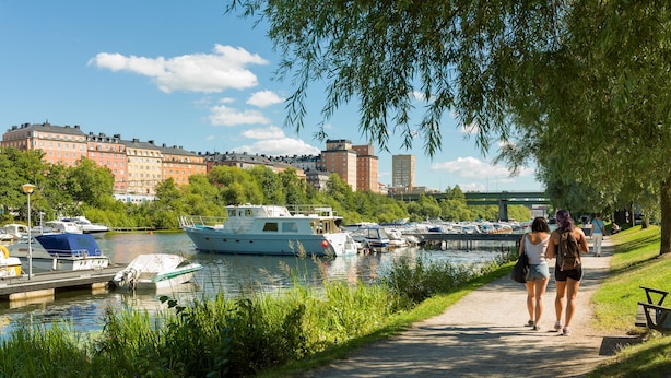 A riverside walkway with boats docked along the river, a bridge in the background, and a path for pedestrians.