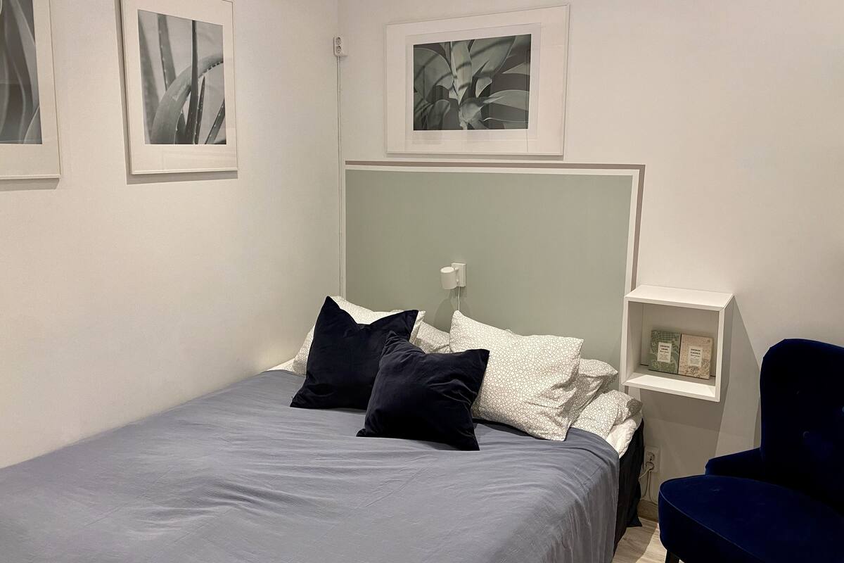 A bedroom with a bed, pillows, a nightstand, a chair, and framed pictures on the wall.