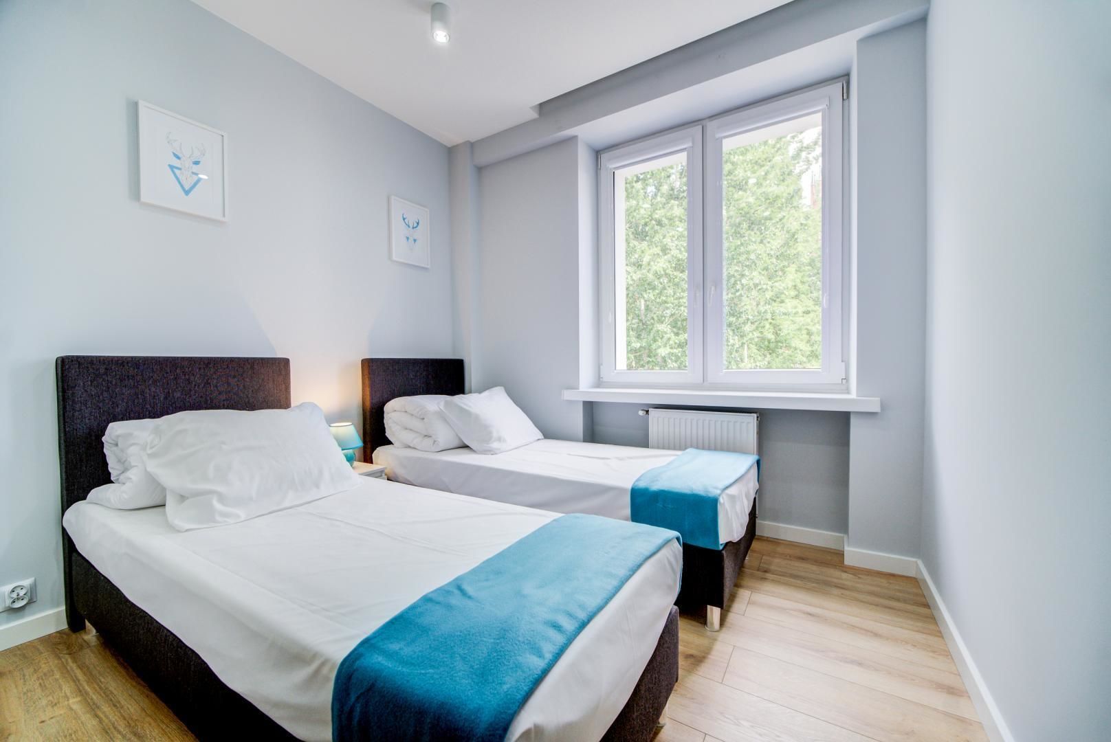 A hotel room with two beds, a window with a view of greenery, and a radiator.