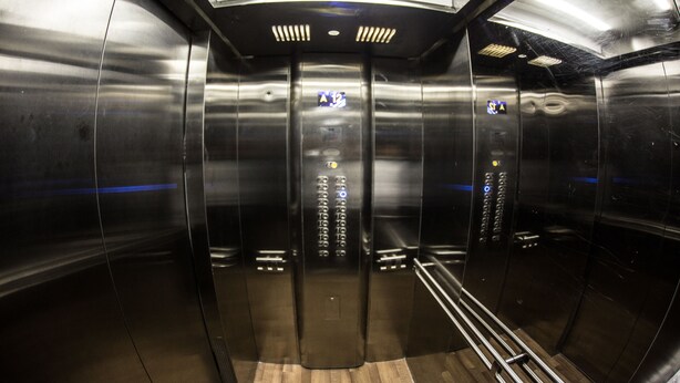 An elevator interior with metallic walls, a wooden floor, and control panels with illuminated buttons. - Bakuvi Tourist Apartment B022 (Baku)