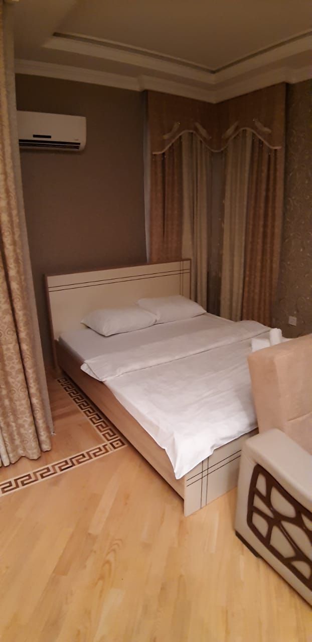A hotel room with a bed, curtains, an air conditioning unit, and a patterned rug.