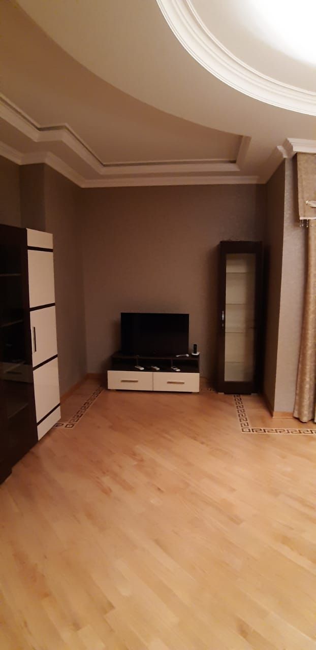 Een kamer met een houten vloer, een flatscreen televisie op een standaard, een kledingkast en een spiegel.