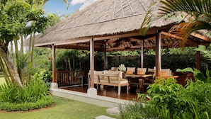 A thatched-roof pavilion with a wooden bench and table, surrounded by lush greenery. - Villa Uma Nina by Nakula (Nusa Dua)