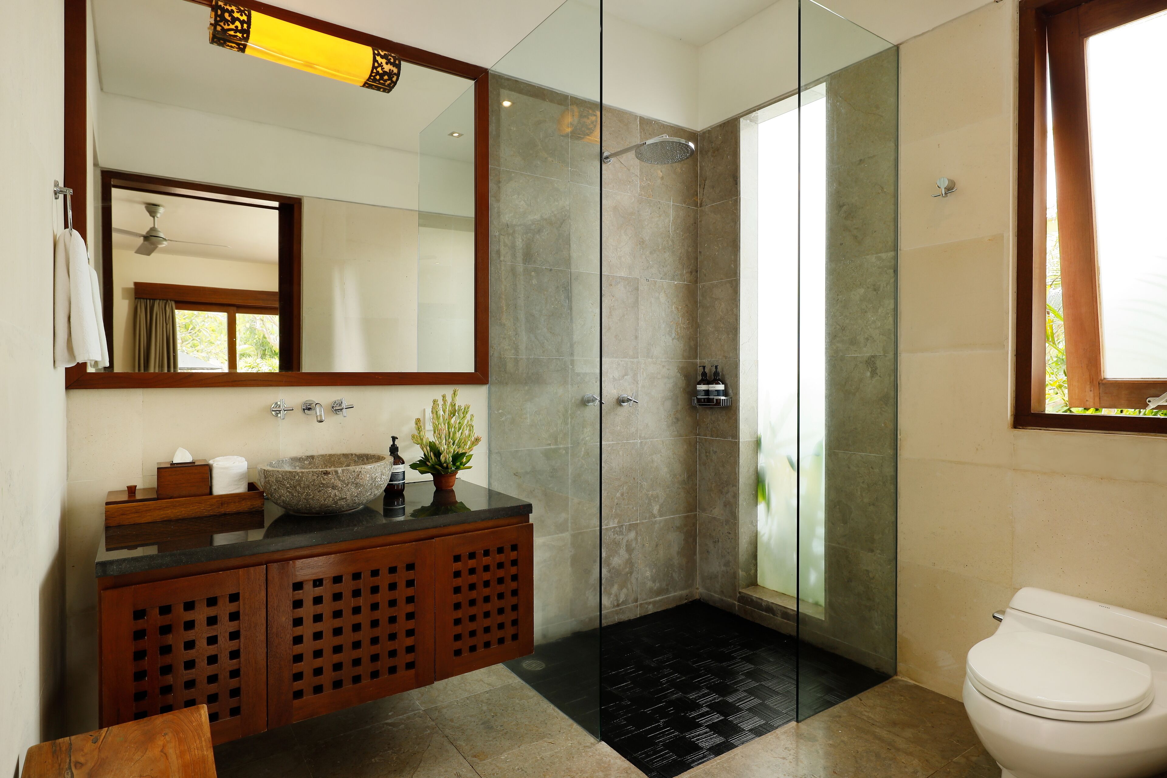 Un baño moderno con ducha envuelta en vidrio, tocador de madera con un lavabo grande y un inodoro.