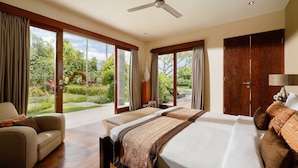A spacious bedroom with a large bed, a sofa, and a view of a lush garden through large sliding doors. - Villa Uma Nina by Nakula (Nusa Dua)