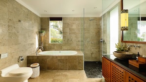 A modern bathroom with a glass-enclosed shower, a freestanding bathtub, and a large mirror with a decorative light fixture. - Villa Uma Nina by Nakula (Nusa Dua)