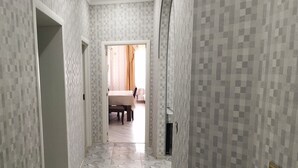 Un pasillo con paredes estampadas y suelo de mármol que conduce a una habitación con cama y sillón.