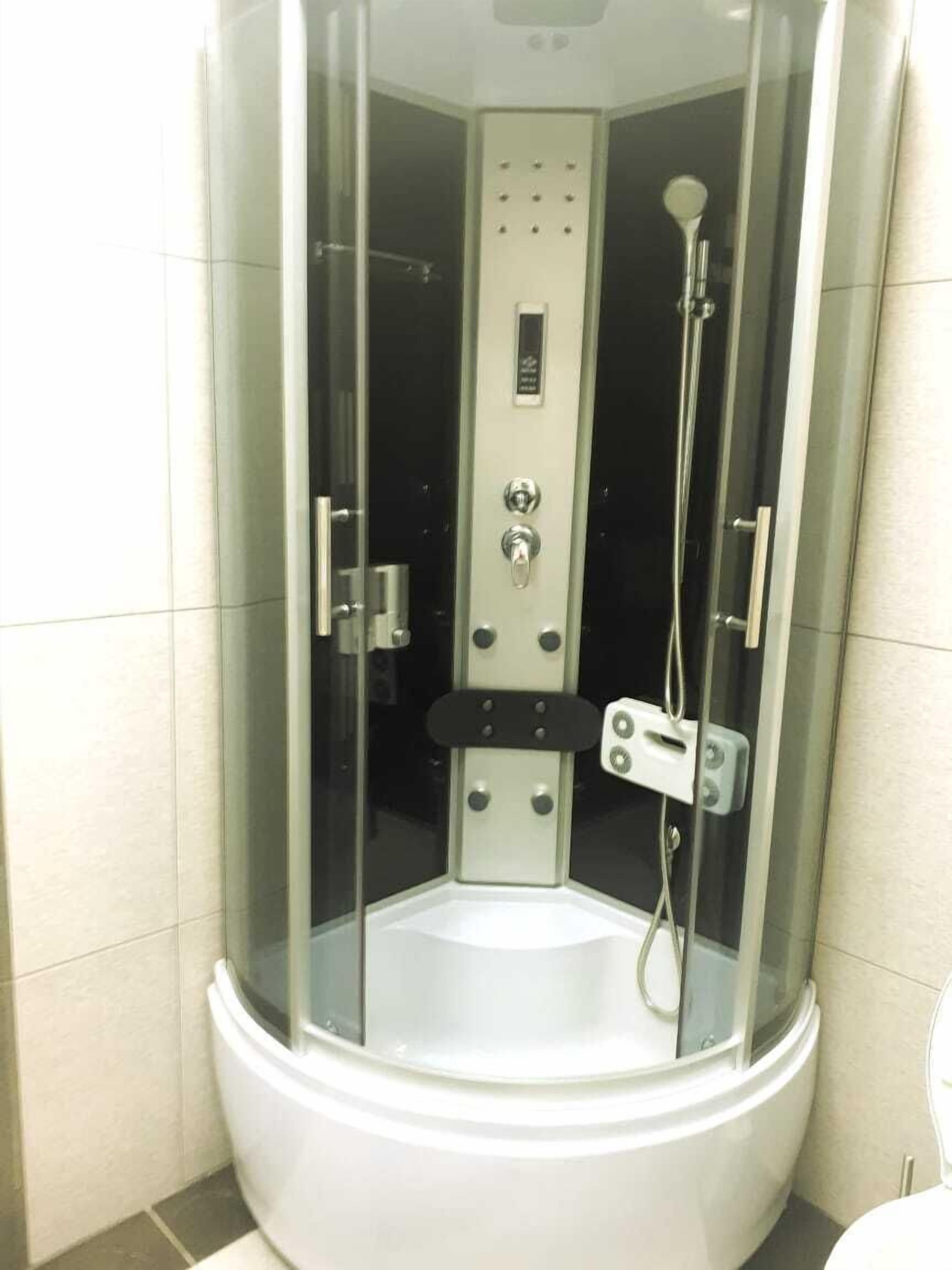 Et brusekabine med glasvægge, et kontrolpanel, en håndholdt brusehoved og en håndholdt massagebruser.