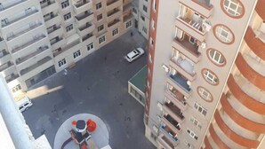 A high-rise building with multiple balconies, a courtyard with a car, and a circular structure with a red object. - Bakuvi Tourist Apartment B098 (Baku)