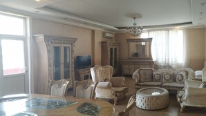 A spacious living room with a large wooden dining table, several upholstered chairs, a round coffee table, and a television. - Apartment 3 rooms 6 Bakuvi (Baku)