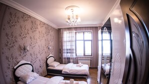 Une chambre d’hôtel avec deux lits, un lustre, une grande fenêtre avec des rideaux et un miroir au mur.
