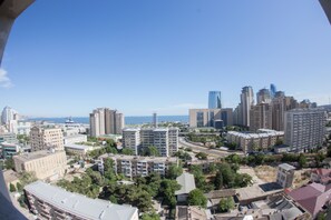 Un paysage urbain composé d’immeubles de grande et de moyenne hauteur, avec un ciel dégagé et une vue sur la mer au loin.