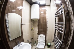 Une salle de bain avec des toilettes, un lavabo et un miroir. On y trouve également un porte-serviettes et un rideau de douche.