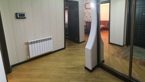 Un couloir avec un radiateur, une caméra de surveillance et un mur recouvert de miroirs qui reflète une pièce contenant un lit et une porte.