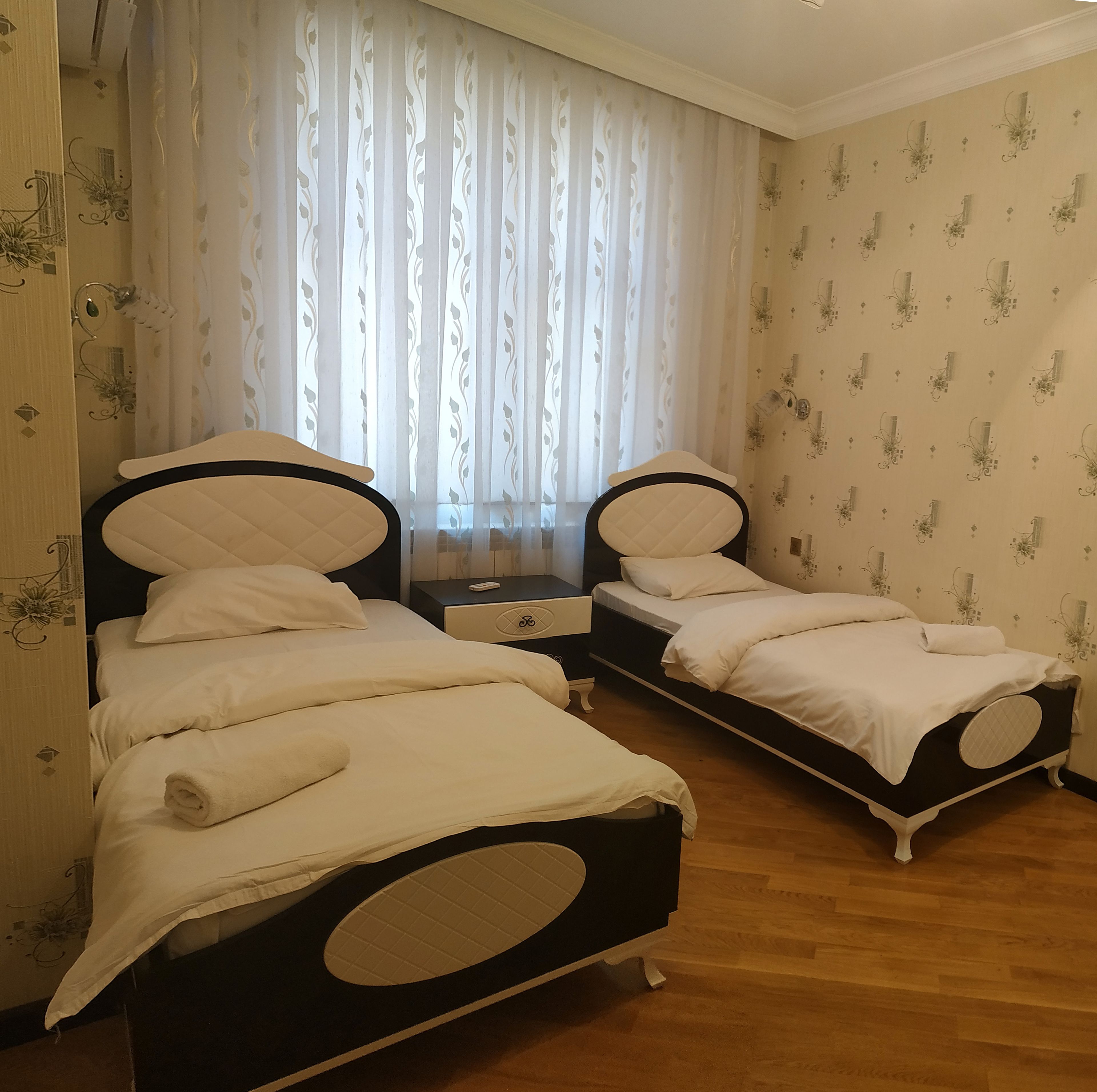 A room with two beds, a nightstand, and a window with curtains.