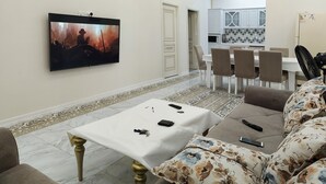 A living room with a flat-screen TV, a sofa, a coffee table, and a dining area with chairs and a table. - Bakuvi Tourist Apartment B097 (Baku)