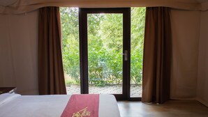 A bedroom with a bed, a red runner, and a view of greenery through a sliding door. - D'Bamboo Kamp (Bintan)