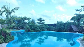 A clear blue swimming pool surrounded by hexagonal tiles, with tropical vegetation and thatched-roof structures in the background. - D'Bamboo Kamp (Bintan)