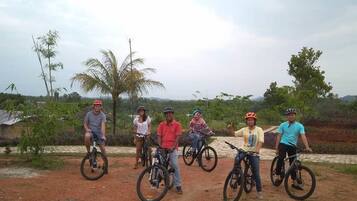 A group of cyclists on a dirt path with palm trees and a rural landscape in the background.