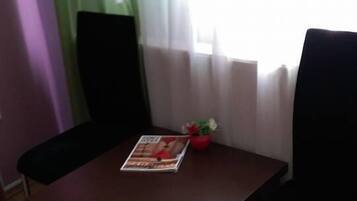 A dining table with two chairs, a magazine on the table, and a small red pot with flowers.