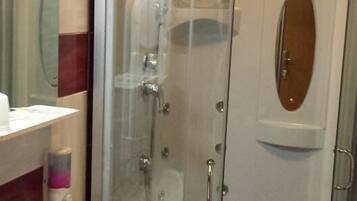 A glass-enclosed shower stall with a handheld showerhead and a handheld faucet.