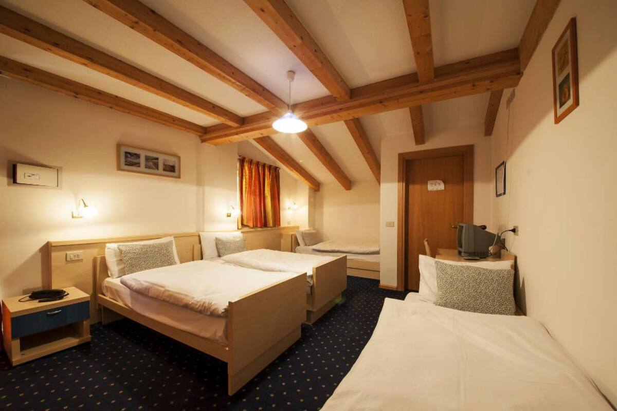 A hotel room with two beds, wooden beams on the ceiling, a television on a side table, and a small desk with a chair.