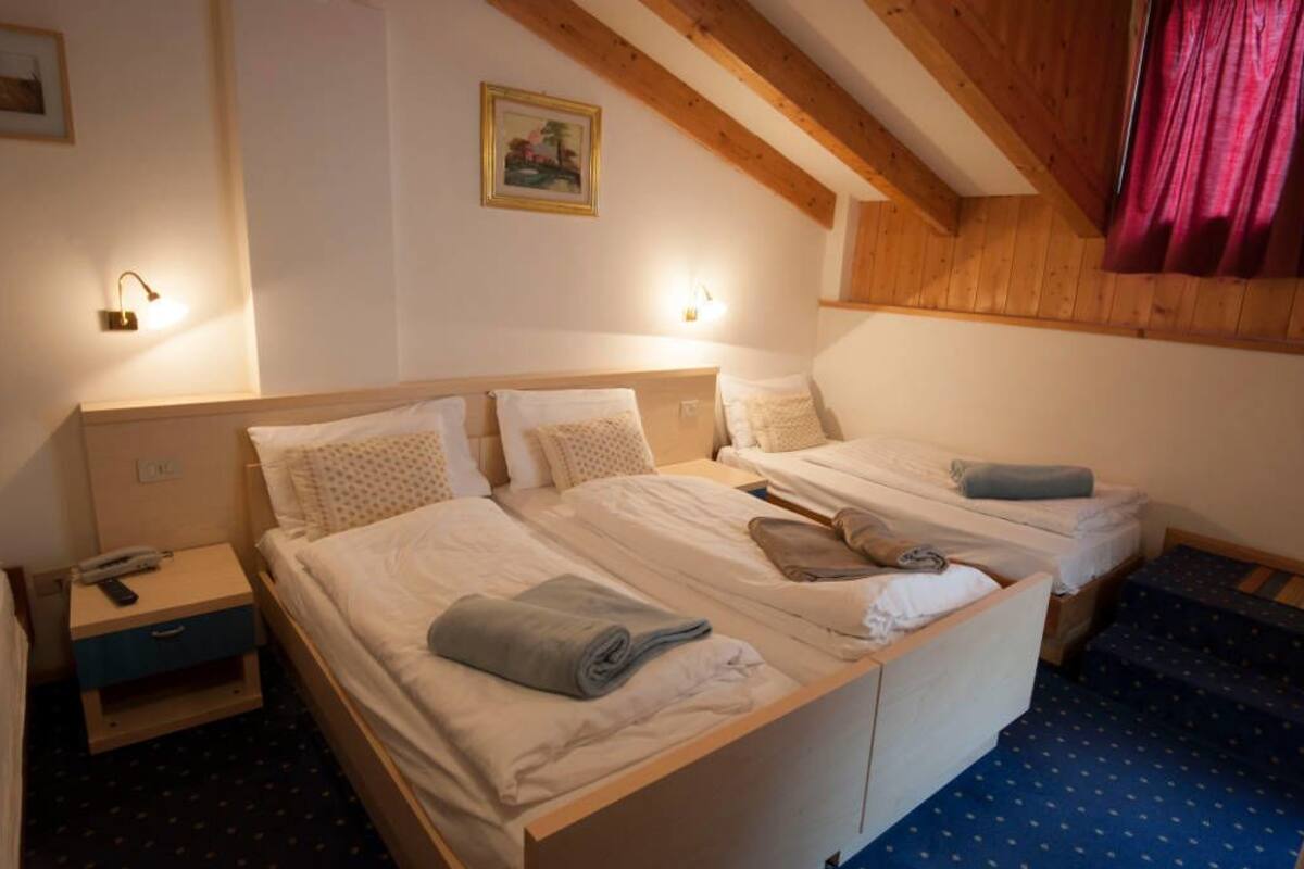A hotel room with two single beds, wooden headboards, a nightstand with a phone, and a painting on the wall.