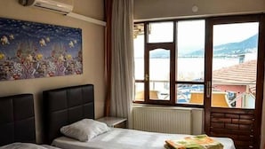 A hotel room with two beds, a large window with a view of the sea, and a painting on the wall. - Seckin Motel (Ayvacik)