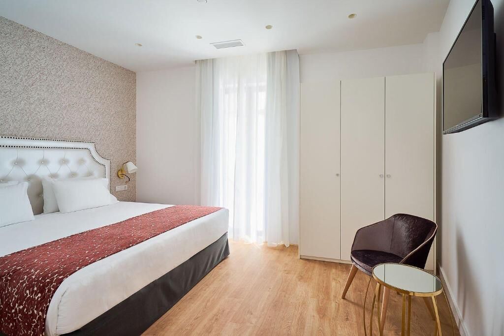 Una habitación de hotel con cama, una silla, armario y televisor en la pared.