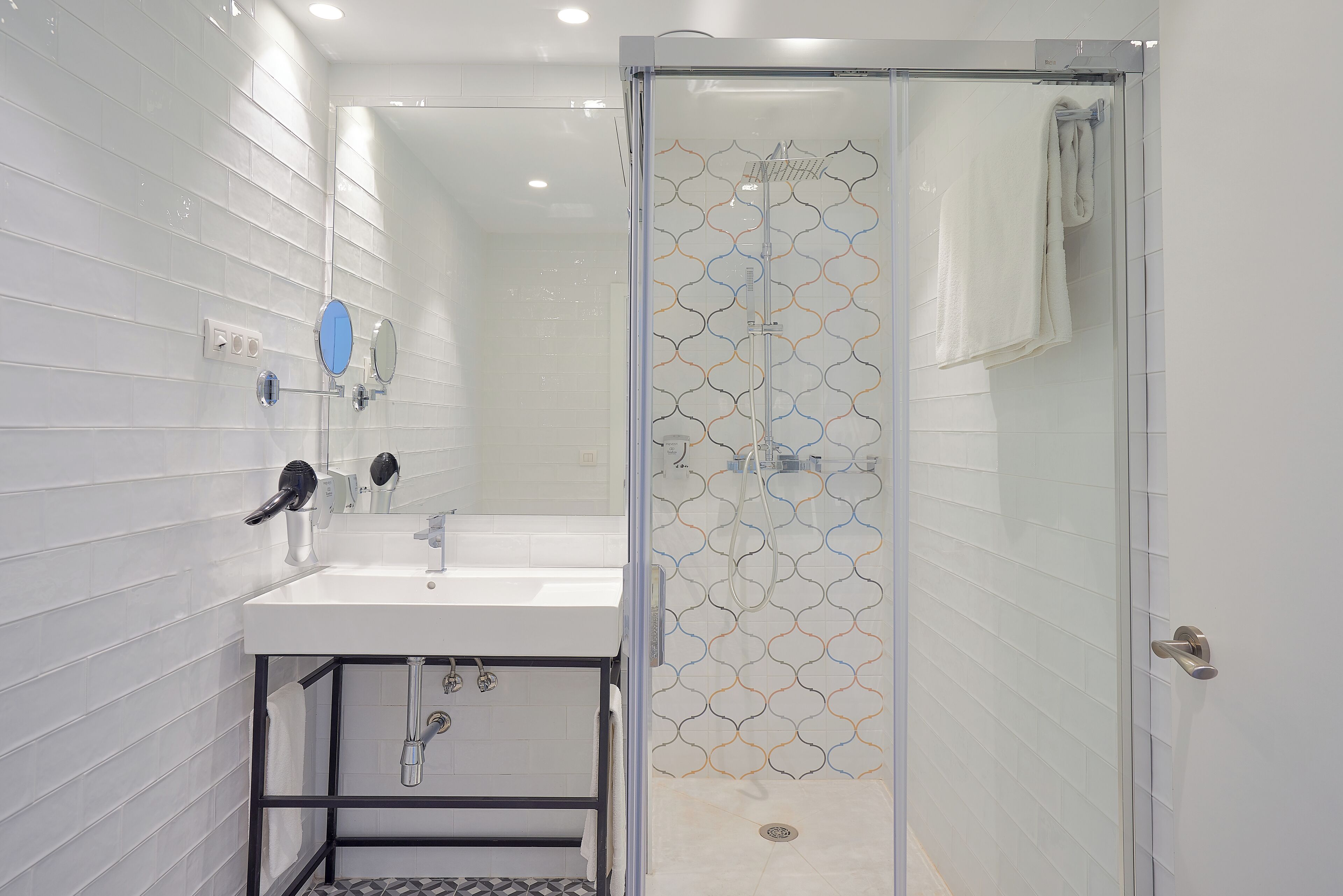 Een moderne badkamer met een douchecabine van glas, een wit wastafelmeubel met een zwart frame, en een betegelde muur met een patroon.
