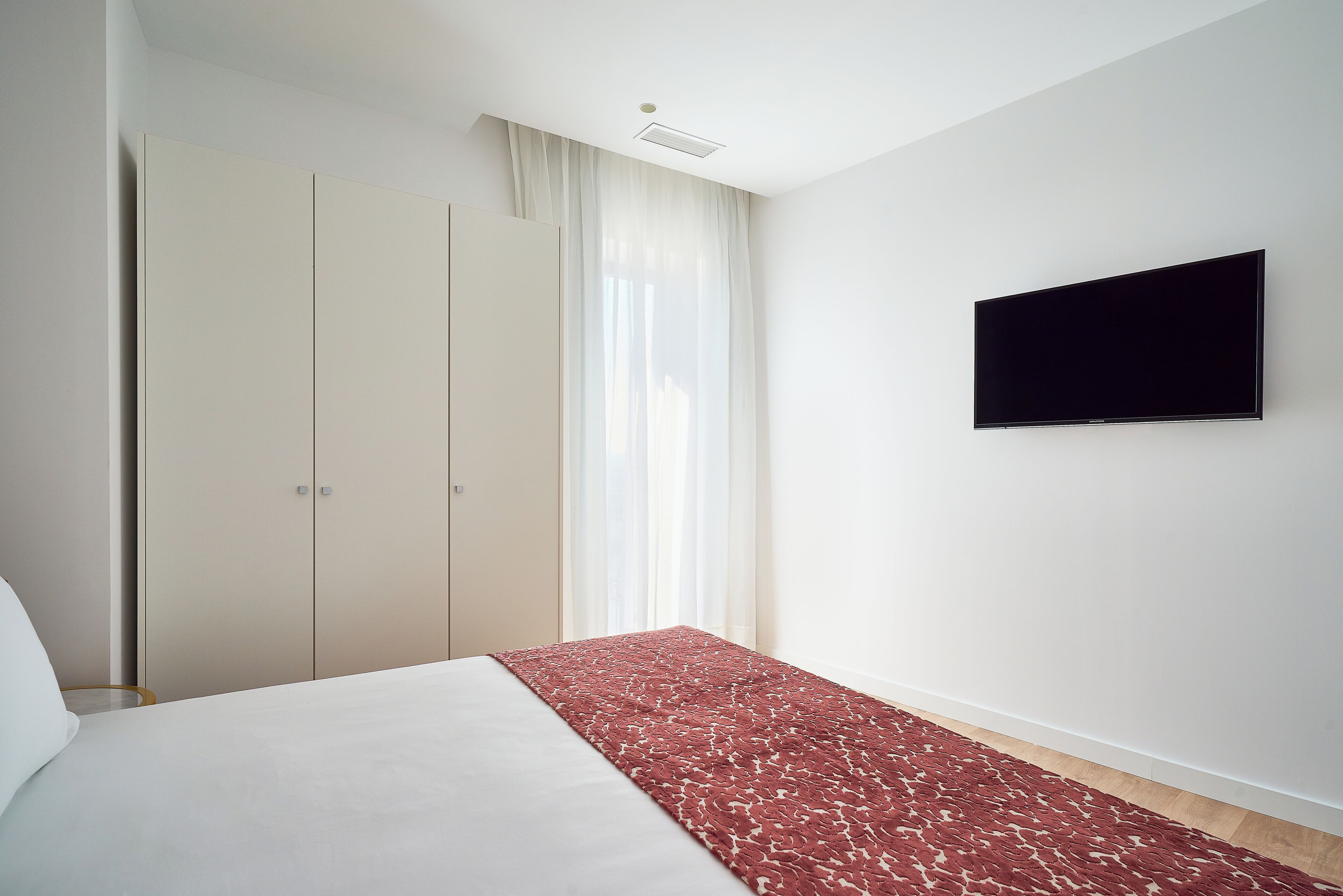 Un dormitorio con cama, televisor montado en la pared y armario.