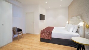 Une chambre d’hôtel moderne, équipée d’un lit, d’une chaise, d’une petite table et d’un téléviseur fixé au mur.