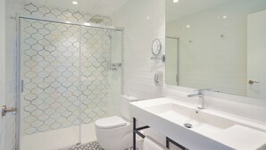 Une salle de bain moderne avec une douche à l’italienne en verre, un lavabo blanc et un grand miroir.
