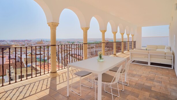 Un balcon avec une table et des chaises blanches, un canapé et une vue sur le paysage urbain.