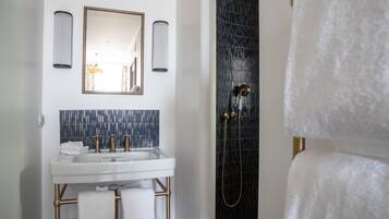 A bathroom with a white sink, gold fixtures, a mirror, and a dark tiled shower area.
