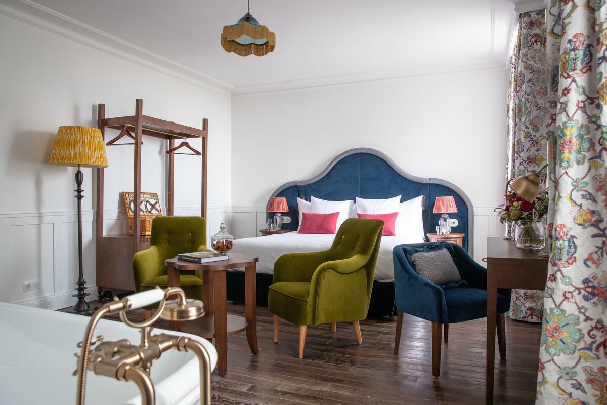 Habitación de hotel con cama, dos sillas, una mesa, una lámpara y una lámpara colgante.