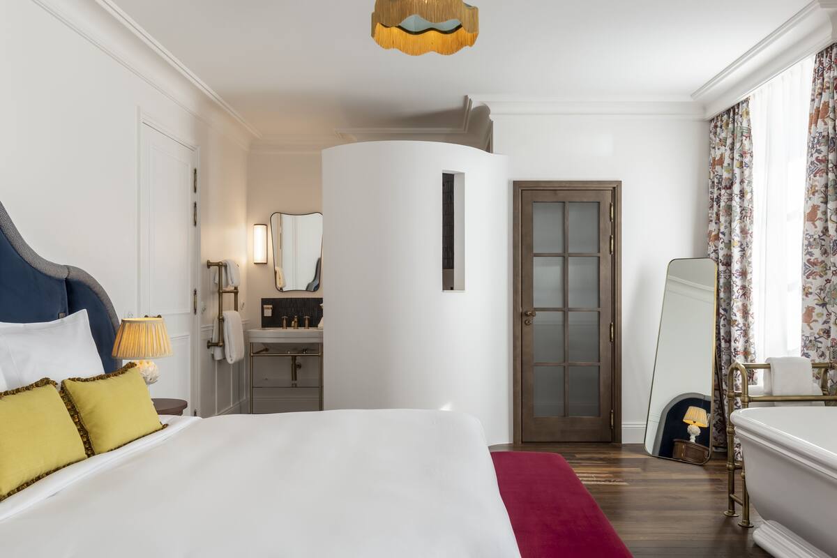 Una habitación de hotel con cama, espejo, baño y puerta.