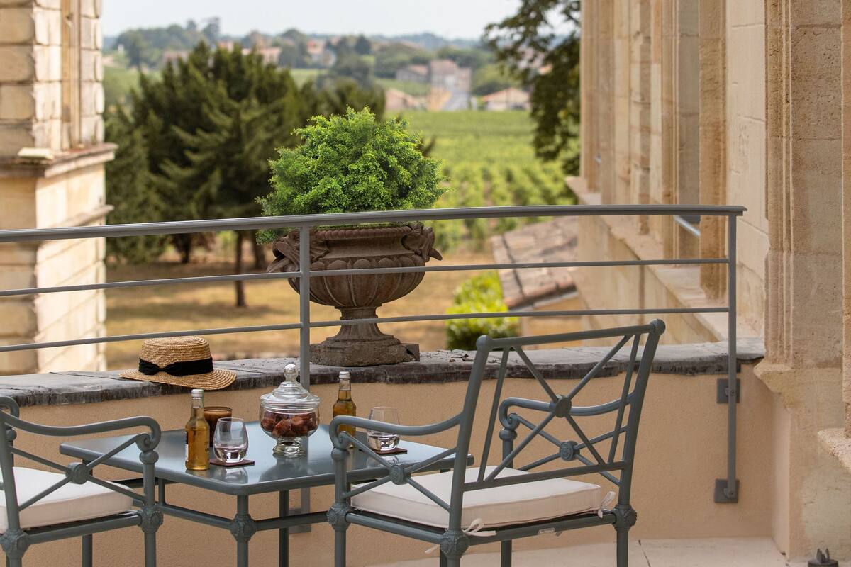 Un balcón con una mesa y sillas, una planta en maceta y vistas a un viñedo.