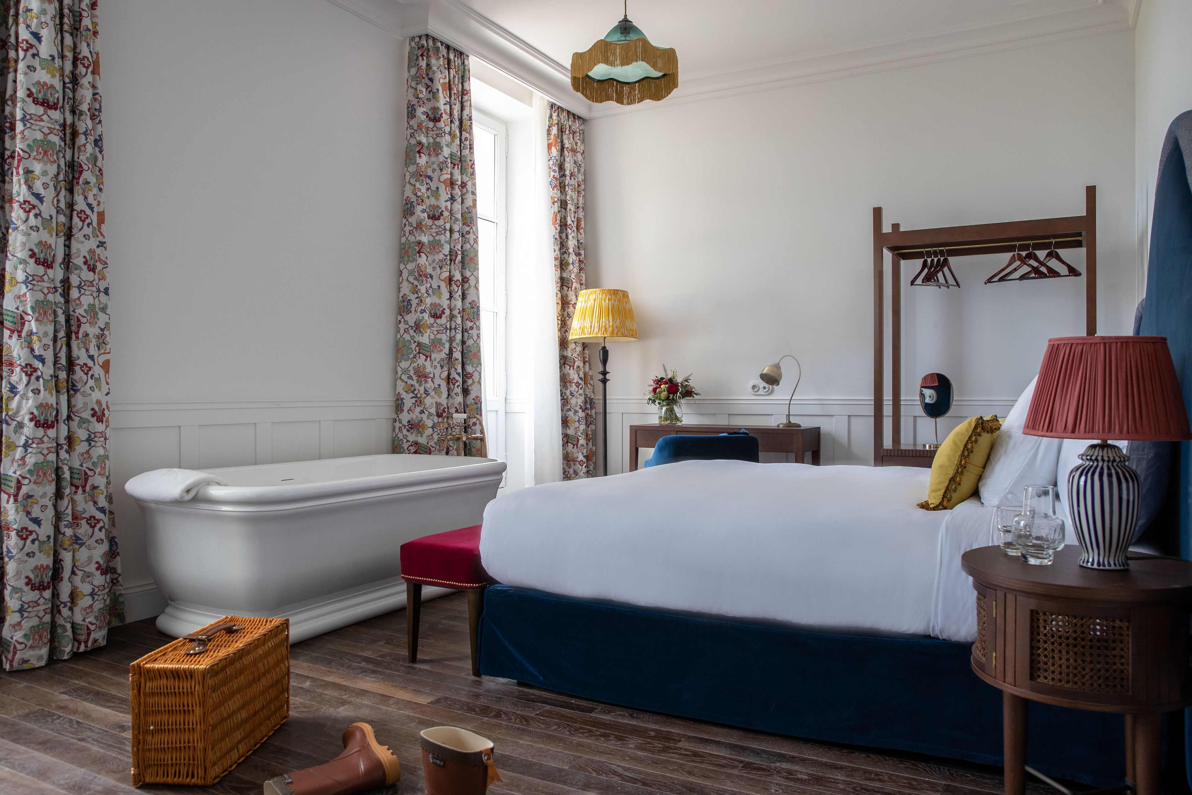 A bedroom with a large bed, a bathtub, a wooden floor, and a dresser.