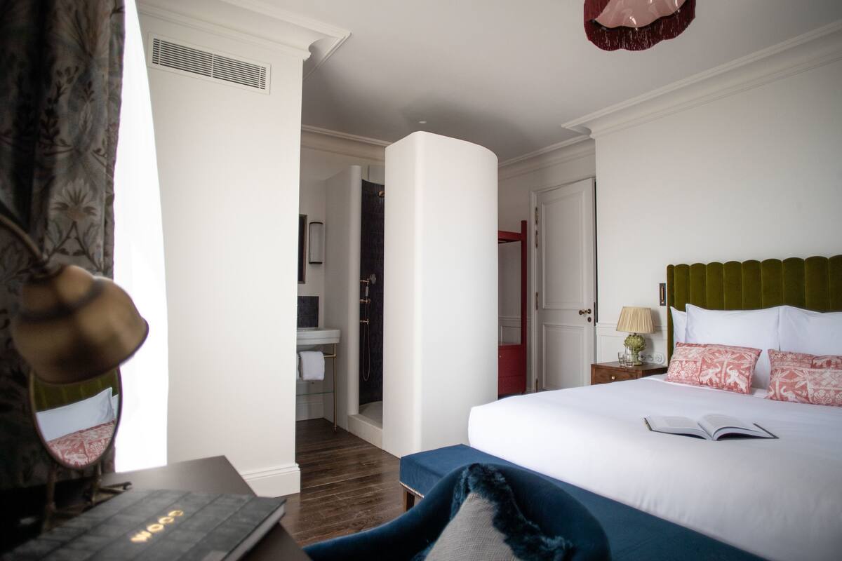 Una habitación de hotel con cama, escritorio con computadora portátil, baño y puerta roja.
