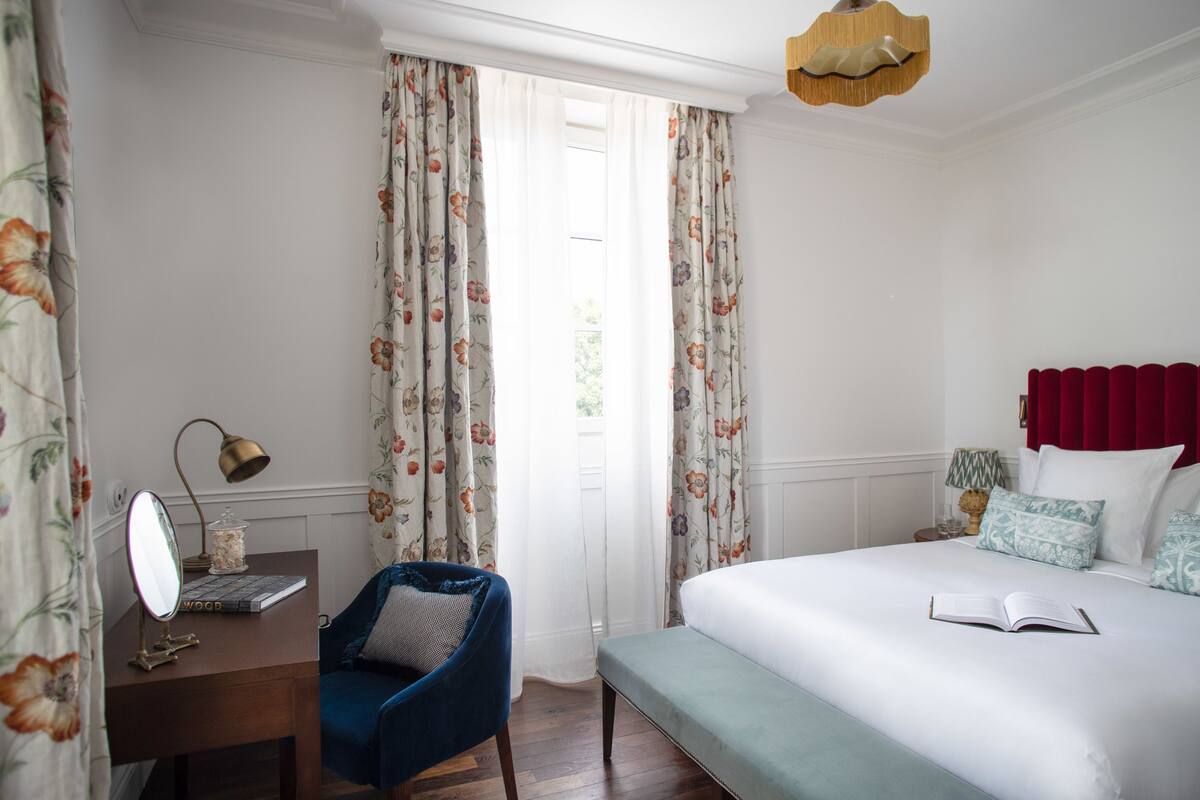 Un dormitorio con cama, escritorio con espejo, silla y ventana con cortinas.