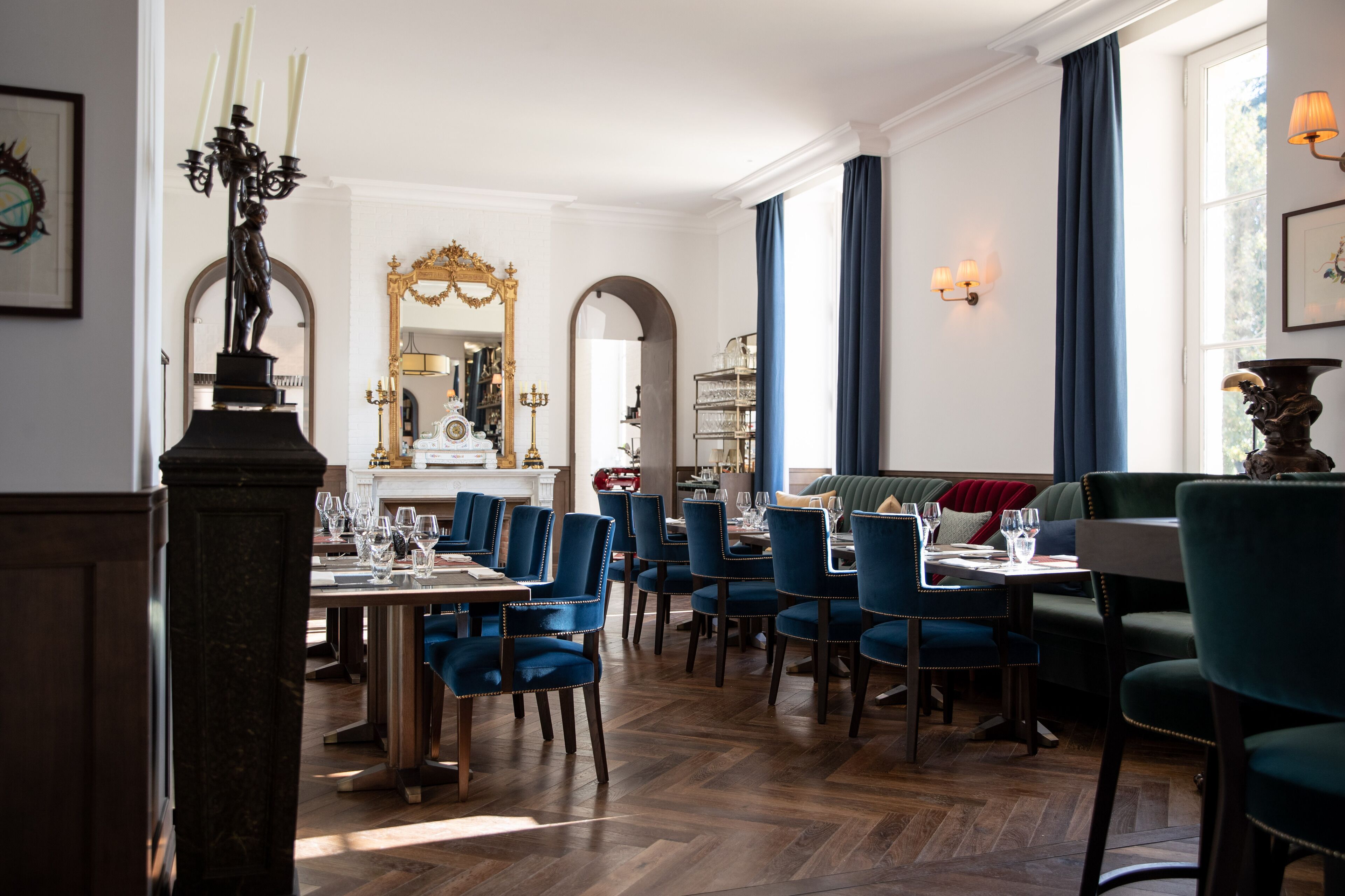 A dining area with blue upholstered chairs, a wooden herringbone floor, and a chandelier.