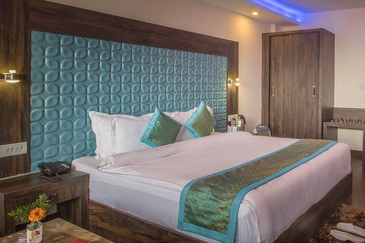 Een moderne hotelkamer met een groot bed, een houten hoofdeinde, een nachtkastje en een bureau met een lamp.